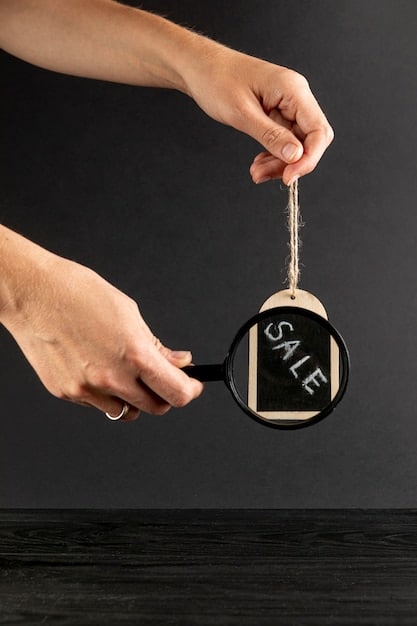 A hand holding a magnifying glass over a price tag that shows both the original price and the discounted price. The background is blurred, emphasizing the scrutiny of the price tag.